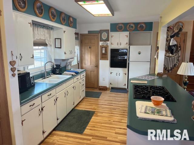 kitchen featuring light wood-style flooring, a sink, black appliances, white cabinetry, and dark countertops