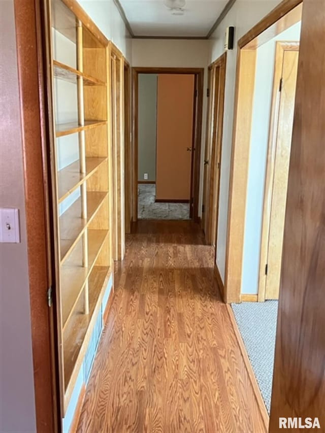 corridor with ornamental molding and wood finished floors