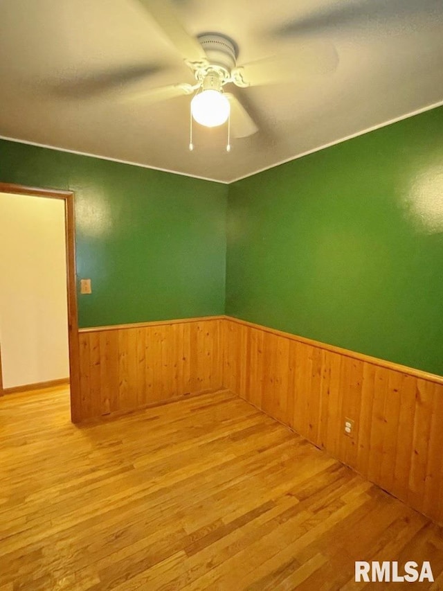 empty room featuring wooden walls, wainscoting, a ceiling fan, and wood finished floors