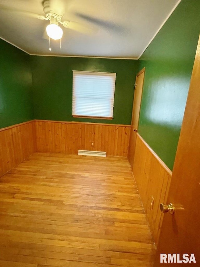 unfurnished room featuring a ceiling fan, wooden walls, wood finished floors, and a wainscoted wall