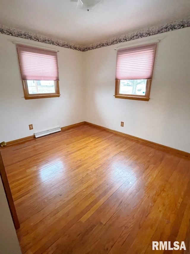 empty room with a baseboard heating unit, baseboards, and wood finished floors