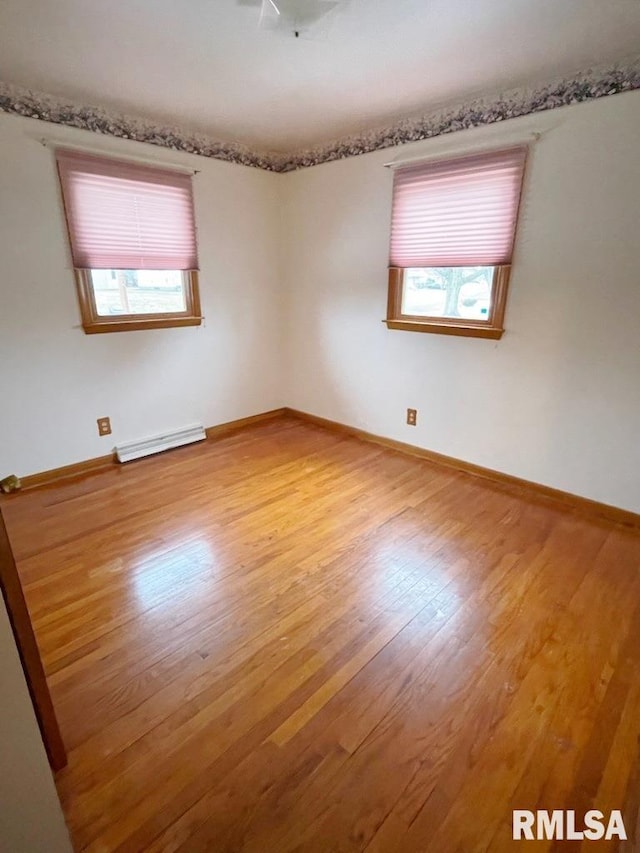 empty room featuring a baseboard radiator, baseboards, and wood finished floors