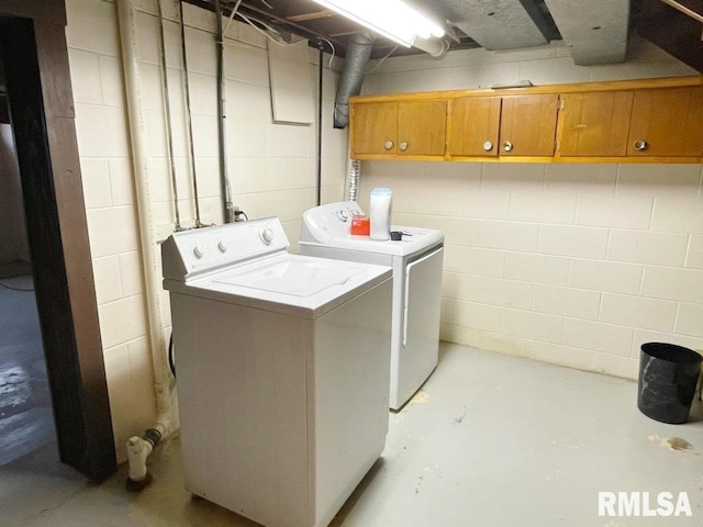 clothes washing area featuring cabinet space, washing machine and dryer, and concrete block wall
