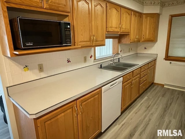 kitchen with black microwave, light countertops, light wood-style flooring, white dishwasher, and a sink