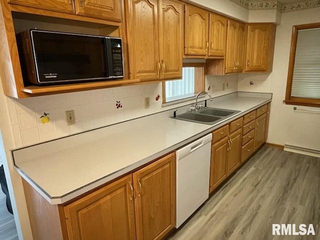 kitchen with light wood-style flooring, a sink, black microwave, white dishwasher, and light countertops