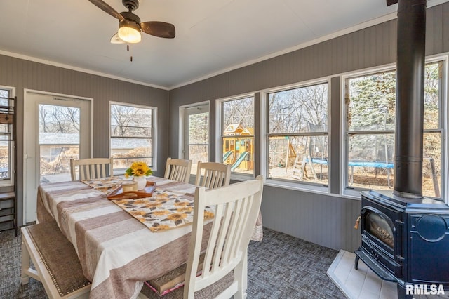 sunroom with a healthy amount of sunlight, a wood stove, and a ceiling fan