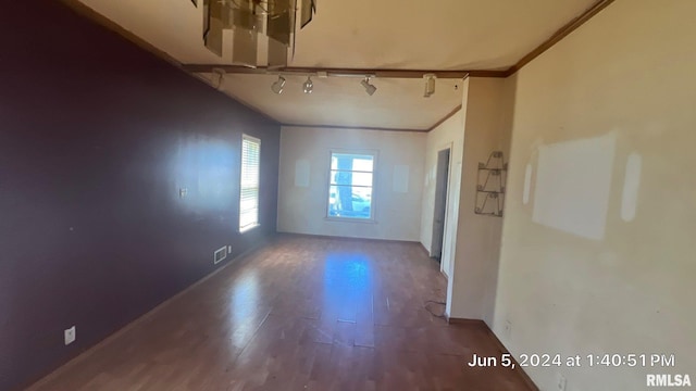 empty room featuring visible vents, track lighting, crown molding, baseboards, and wood finished floors