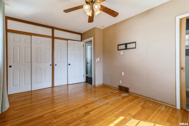 unfurnished bedroom with visible vents, ceiling fan, light wood-style floors, and multiple closets