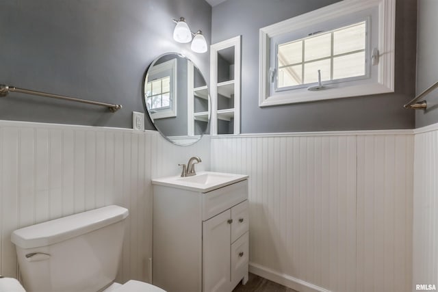 half bath with a wainscoted wall, toilet, and vanity