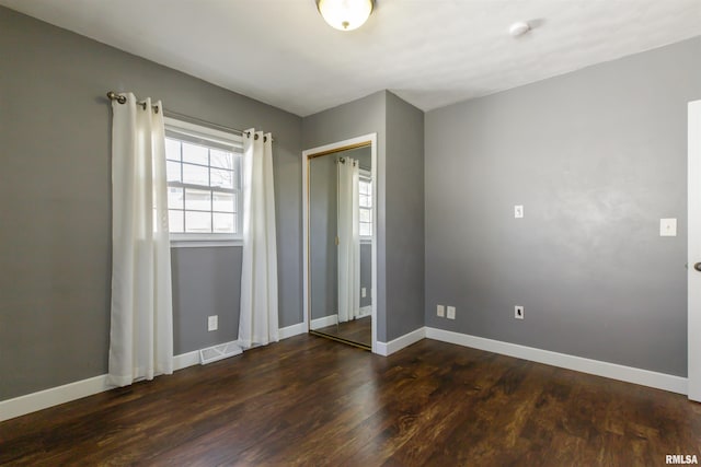 unfurnished bedroom with a closet, baseboards, and dark wood-style flooring