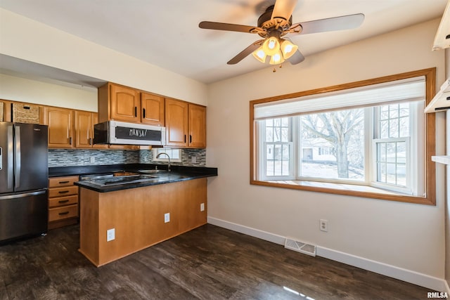 kitchen with visible vents, a sink, freestanding refrigerator, brown cabinetry, and white microwave