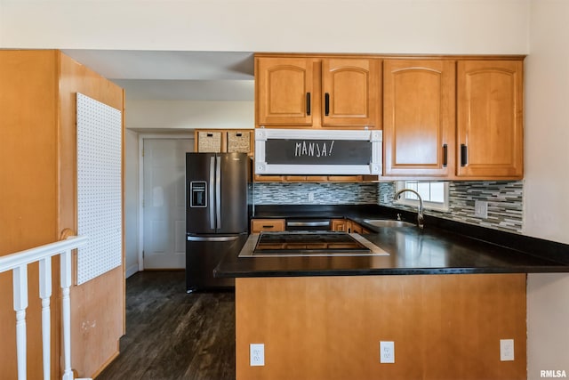 kitchen with fridge with ice dispenser, a sink, dark countertops, stovetop, and a peninsula