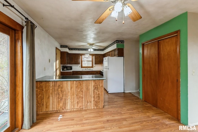 kitchen featuring a peninsula, light wood-style flooring, freestanding refrigerator, a sink, and black microwave