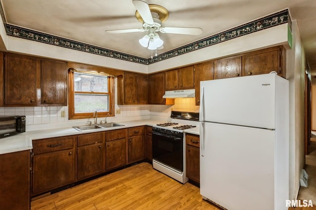 kitchen with a sink, under cabinet range hood, range with gas stovetop, freestanding refrigerator, and light countertops