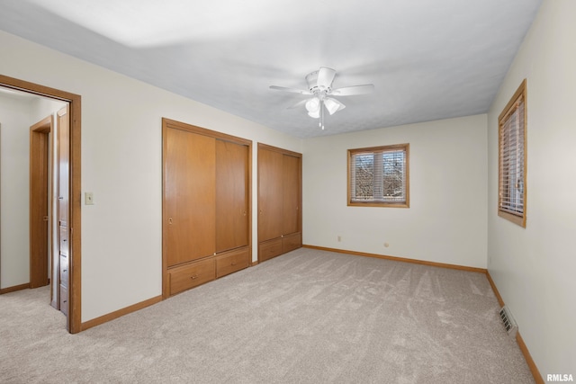 unfurnished bedroom featuring a ceiling fan, baseboards, visible vents, light carpet, and two closets