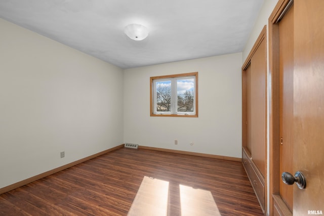 unfurnished bedroom with dark wood-style floors, visible vents, a closet, and baseboards