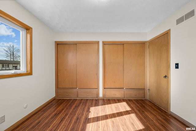 unfurnished bedroom with visible vents, baseboards, two closets, and dark wood-style flooring