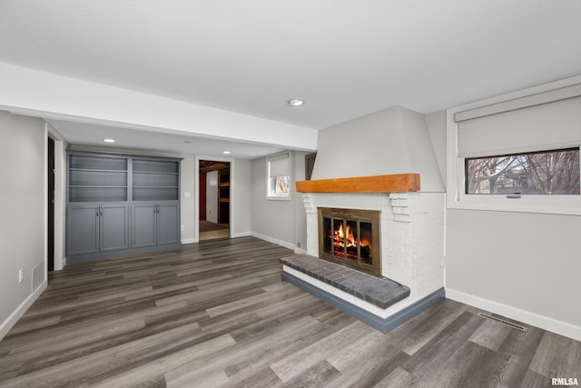 unfurnished living room featuring visible vents, wood finished floors, recessed lighting, baseboards, and a brick fireplace