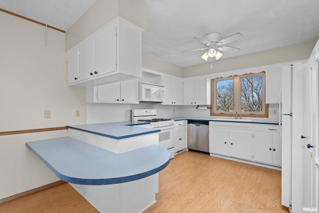 kitchen featuring a sink, white appliances, a peninsula, white cabinets, and light wood finished floors