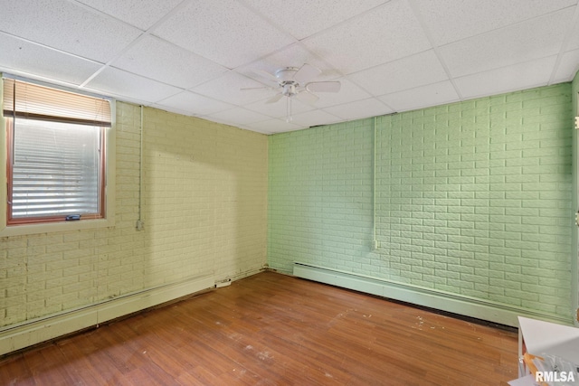 unfurnished room with wood finished floors, a baseboard radiator, a paneled ceiling, and brick wall