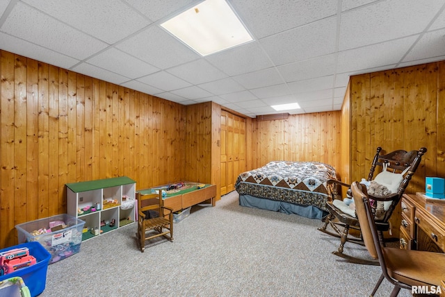 carpeted bedroom featuring wood walls and a paneled ceiling