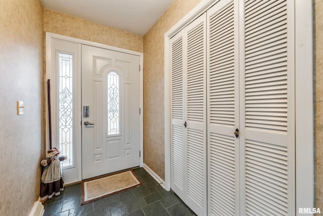 foyer entrance featuring stone finish flooring, baseboards, and wallpapered walls