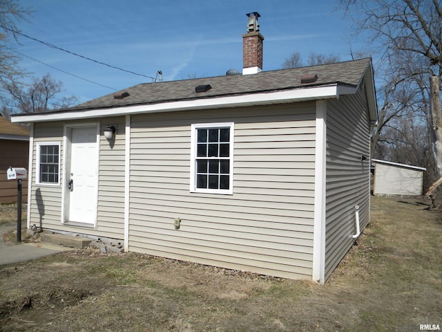 rear view of property featuring a chimney and a shingled roof