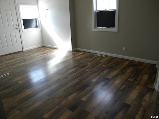 unfurnished room with visible vents, baseboards, and dark wood-style flooring