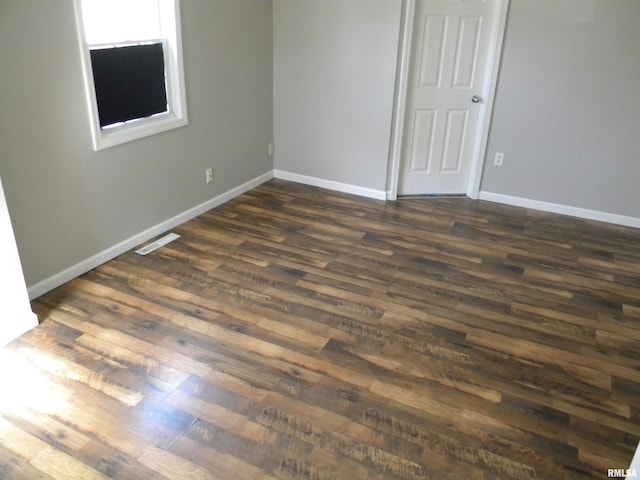 unfurnished room with dark wood-type flooring, visible vents, and baseboards