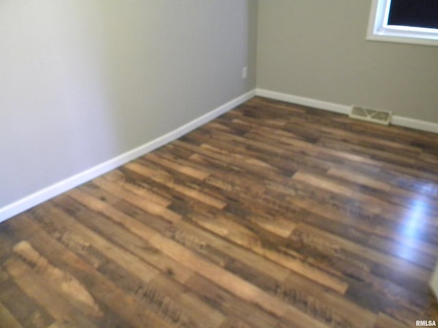 empty room featuring visible vents, dark wood-type flooring, and baseboards