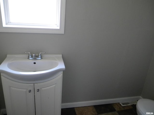 half bath with vanity, toilet, visible vents, and baseboards