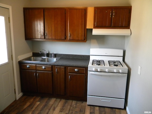 kitchen with a sink, under cabinet range hood, gas range gas stove, dark countertops, and dark wood-style flooring