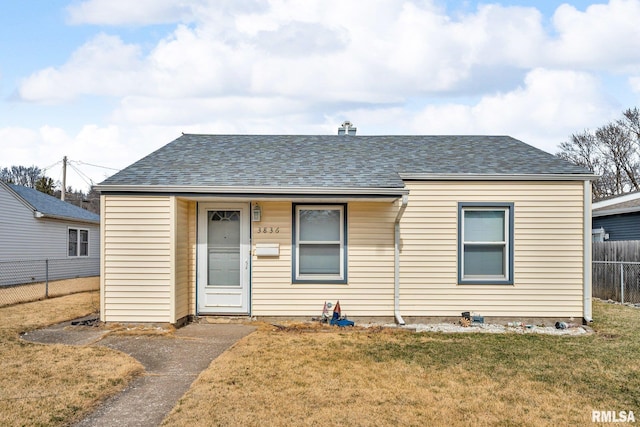 bungalow-style home with a shingled roof, a front lawn, and fence