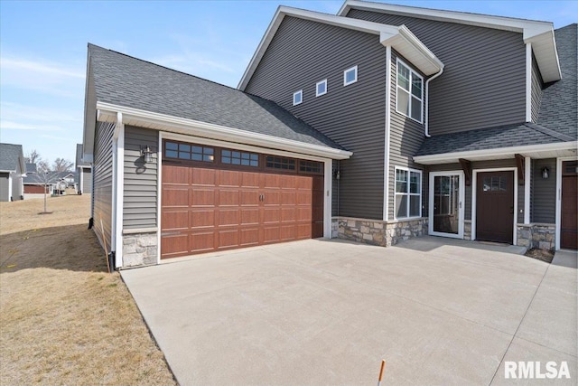 view of front facade featuring a garage, stone siding, driveway, and a shingled roof