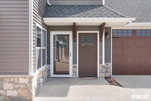 property entrance featuring stone siding, a garage, and roof with shingles