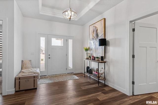 foyer entrance featuring baseboards, a raised ceiling, dark wood-type flooring, and an inviting chandelier