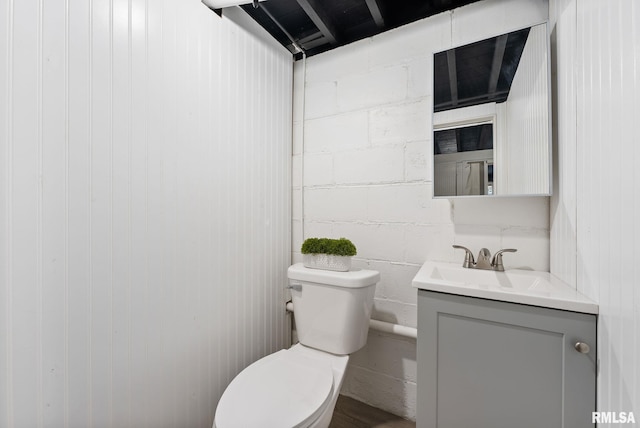 bathroom featuring vanity, concrete block wall, and toilet