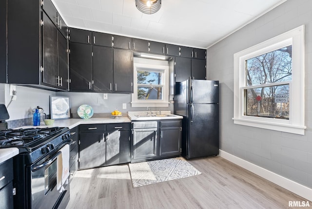 kitchen with black appliances, a sink, light wood-style floors, light countertops, and dark cabinets