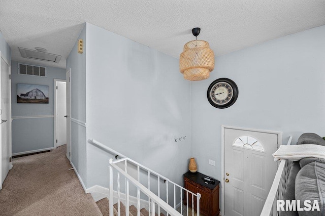 interior space featuring visible vents, a textured ceiling, carpet flooring, baseboards, and attic access