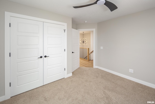 unfurnished bedroom with a closet, carpet flooring, ceiling fan with notable chandelier, and baseboards