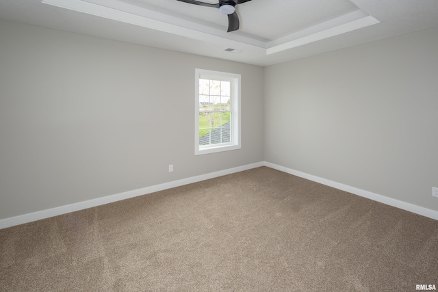 carpeted empty room featuring a ceiling fan, a raised ceiling, visible vents, and baseboards