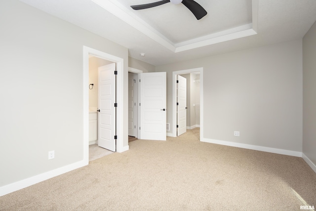 unfurnished bedroom featuring baseboards, a raised ceiling, light colored carpet, and a spacious closet