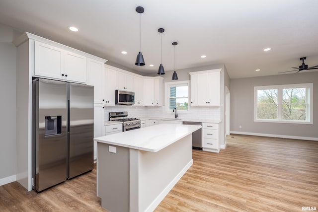 kitchen with light wood finished floors, decorative backsplash, stainless steel appliances, white cabinetry, and a sink