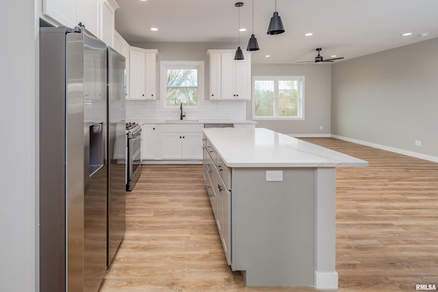 kitchen featuring light wood-style flooring, a sink, appliances with stainless steel finishes, tasteful backsplash, and a center island