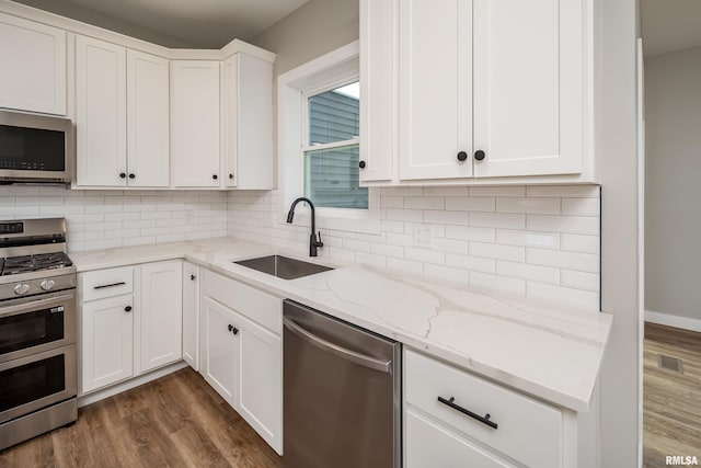 kitchen with dark wood-type flooring, decorative backsplash, stainless steel appliances, white cabinetry, and a sink