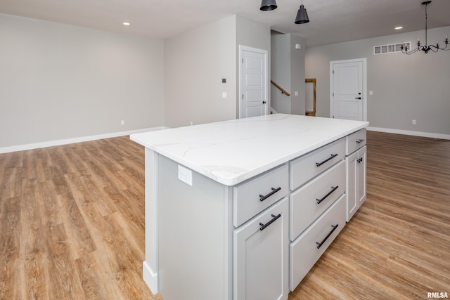 kitchen with a center island, white cabinets, light wood finished floors, baseboards, and hanging light fixtures