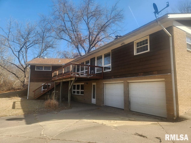 rear view of property featuring stairway, concrete driveway, an attached garage, a wooden deck, and brick siding