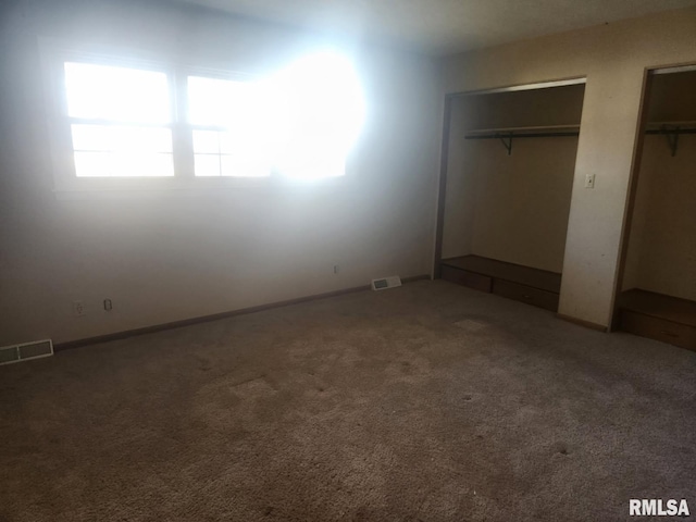 unfurnished bedroom featuring carpet flooring, visible vents, and multiple closets