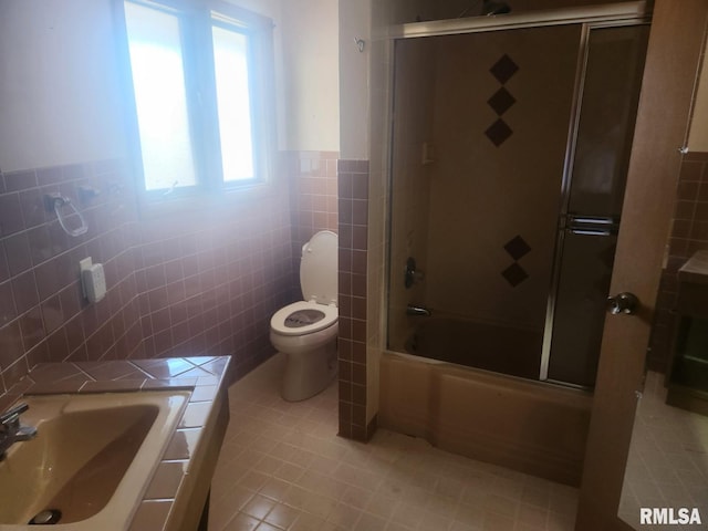 bathroom with bath / shower combo with glass door, a sink, tile walls, toilet, and tile patterned floors