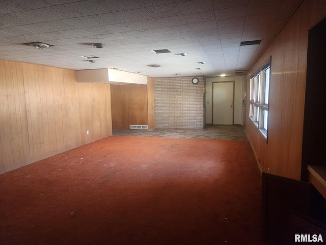 basement featuring visible vents, wooden walls, and carpet flooring